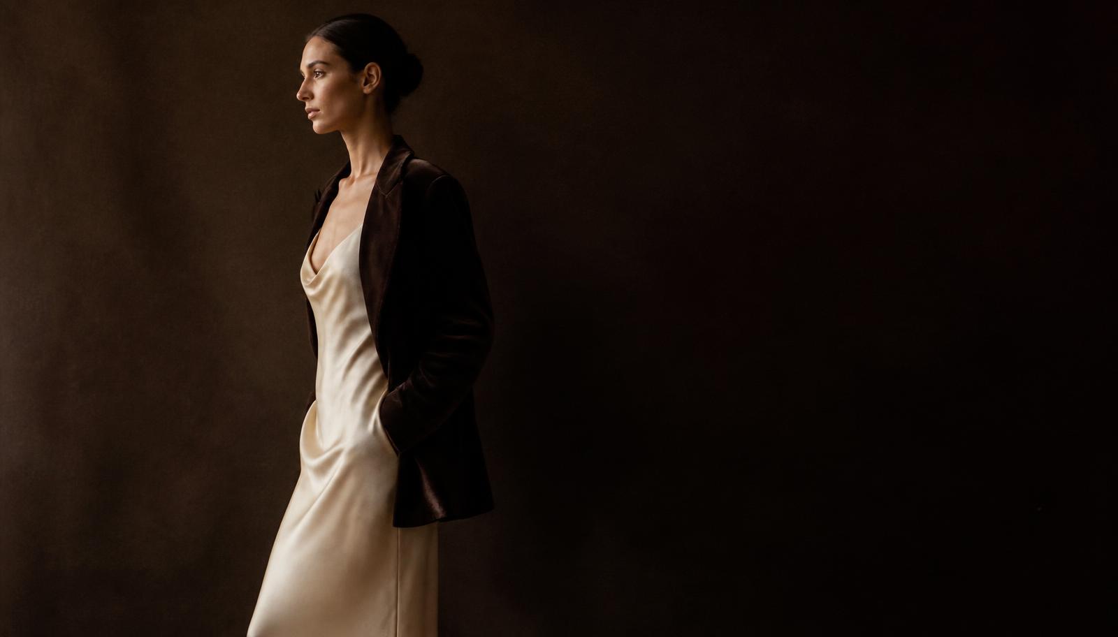 A woman in a cream silk slip dress and dark velvet jacket